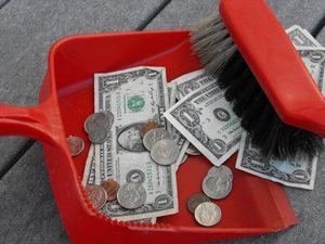 Dollar bills and change swept up in a red dustpan