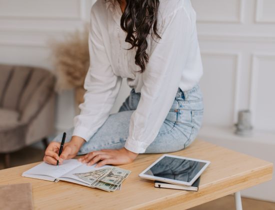 Woman sitting at desk with money and notebook working on her budget.