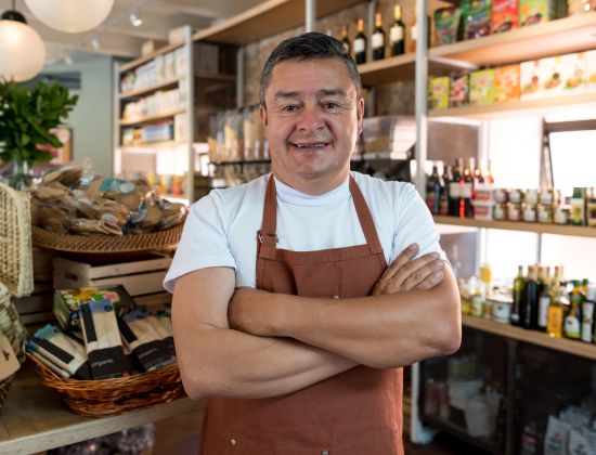 Male small business owner standing in shop with apron on smiling.