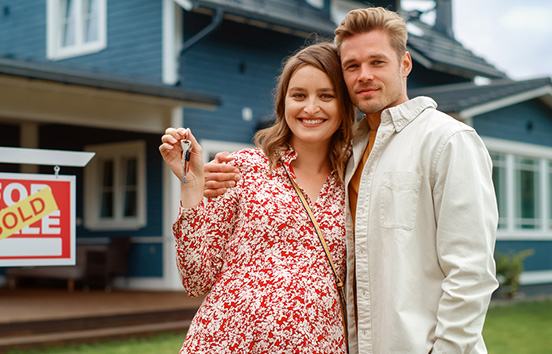 Happy couple standing with keys in front of new home.