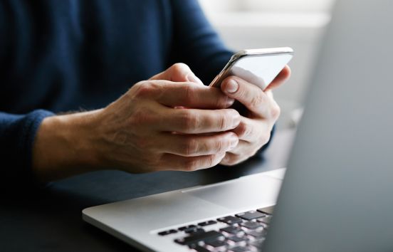 Hands on cell phone with laptop in foreground looking at external accounts