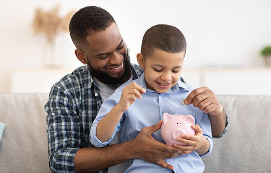 Father and son on couch putting change in piggy bank learning about Financial Literacy