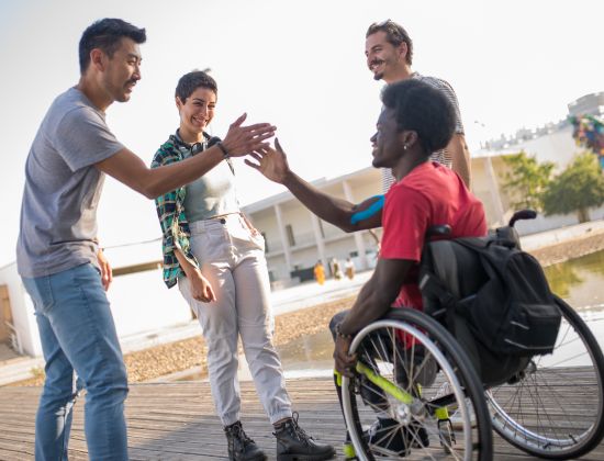 Group of young adults smiling outside. Two giving each other a high-five.