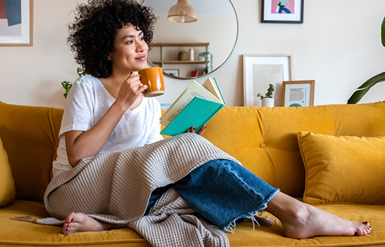 Woman on her couch reading and having coffee