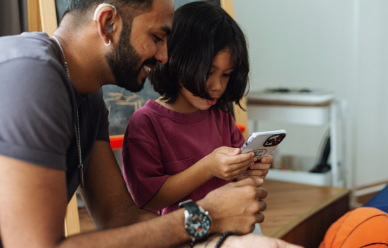 Man with hearing aid looking at phone with sonMan with hearing aid holding phone with son