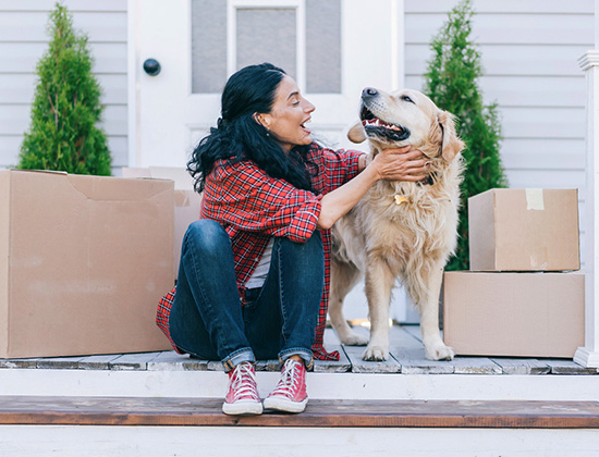 Мid adult woman moving to new house and sitting on the stairs and petting her golden retriever