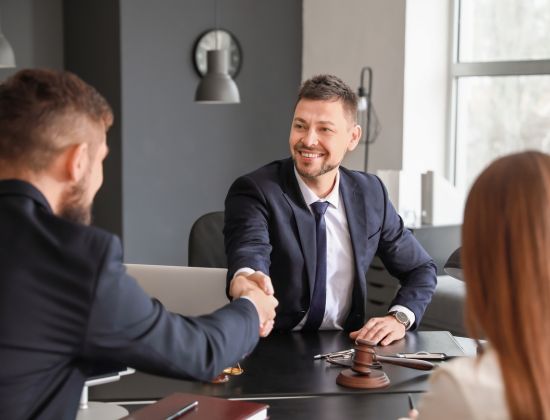 Male attorney shaking client's hand at desk. 