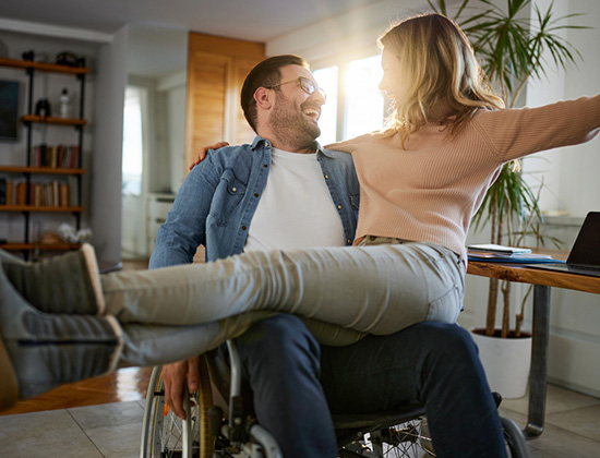 Happy woman talking to her disabled boyfriend while sitting in his lap at home.