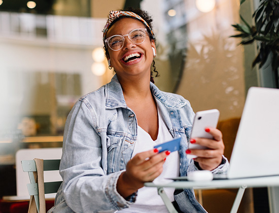 Woman at cafe at laptop with mobile phone and credit card in hand