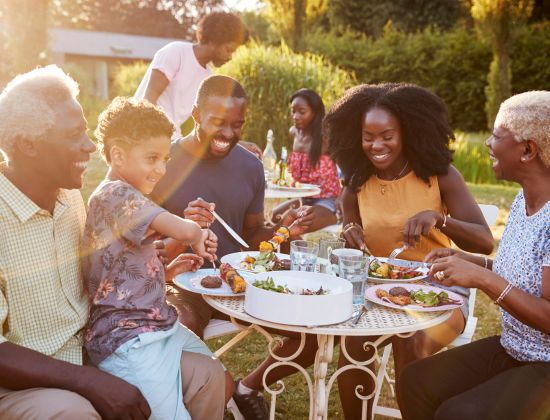 Multigeneration family eating together outside on a sunny day.