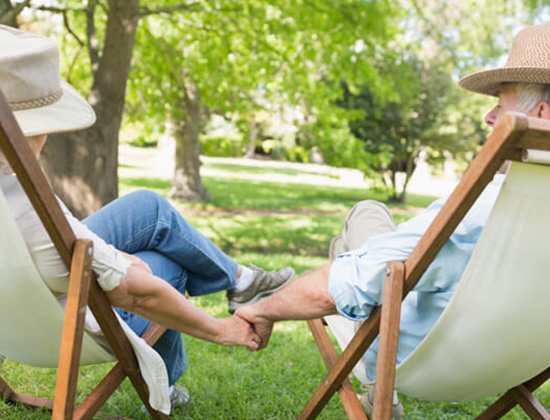 Older couple in park in chairs holding hands
