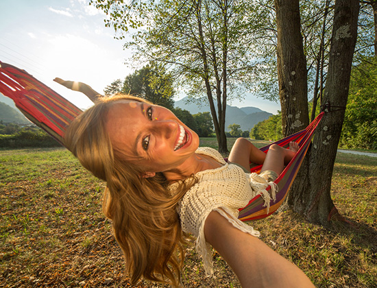 Young woman relaxing on hammock in summer taking a selfie using a mobile phone.