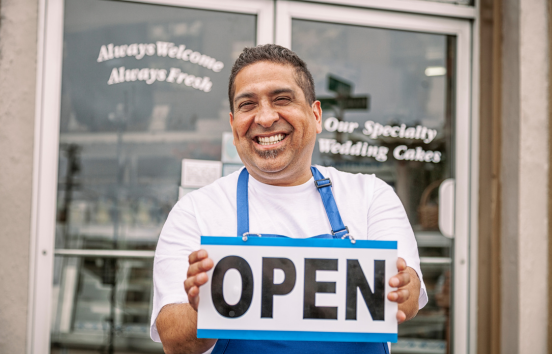 Bakery business owner holding an open sign out front of his store.