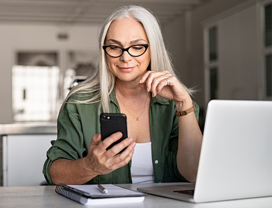 Older woman business owner at desk on cell phone and laptop