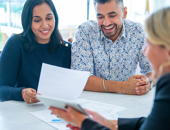 Couple meeting with MIDFLORIDA Mortgage Specialist. They are sitting at desk with documents and a digital tablet presentation.
