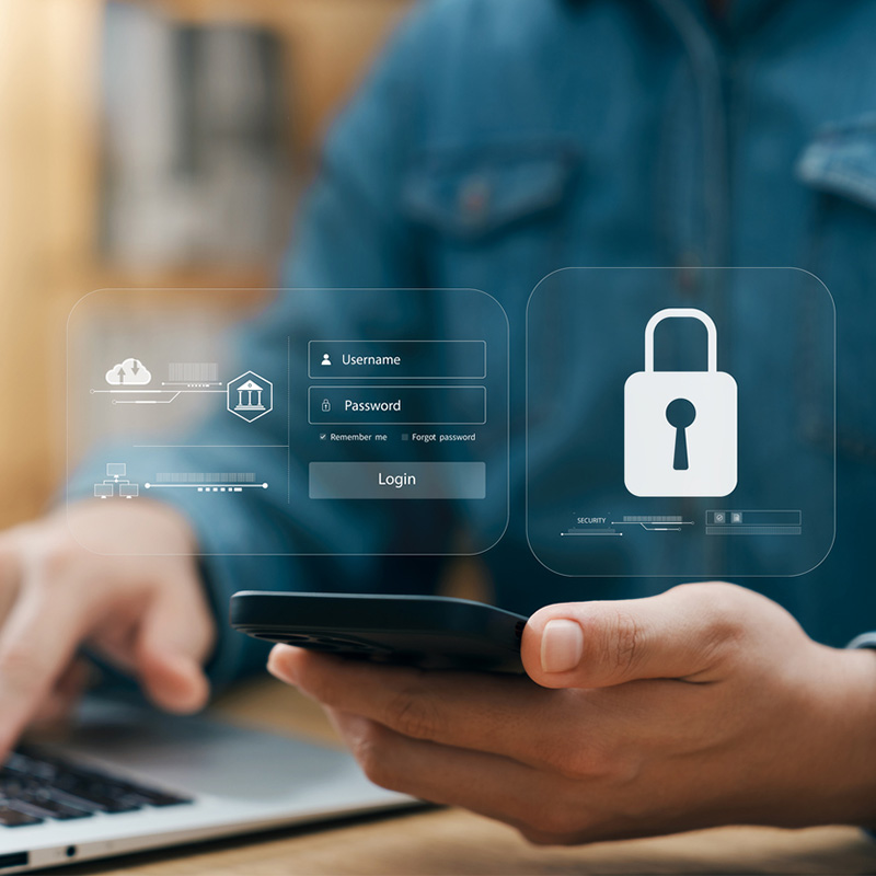 Male at laptop with cell phone with fraud protection symbols on screen