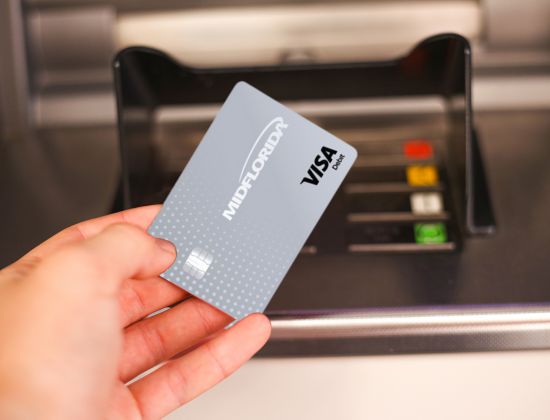 Hand holding a gray Visa debit card at payment machine. 