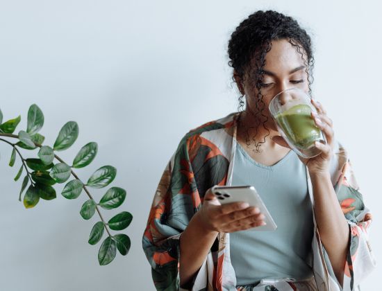 Female drinking matcha tea looking at mobile phone checking her direct deposit