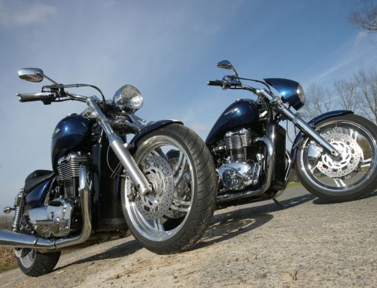 Two motorcycles parked next to one another on gravel