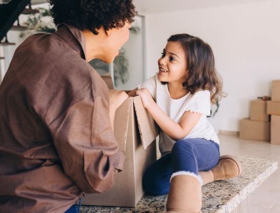 Mom and young daughter unpacking box in kitchen