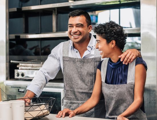 Man and woman wearing aprons, working in the kitchen of a restaurant.