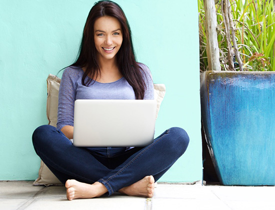 Woman in 20s leaning on blue wall using laptop