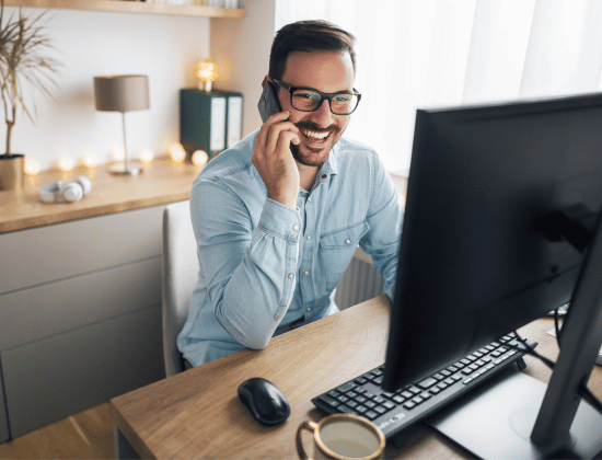 Man on phone sitting at desk behind their computer.