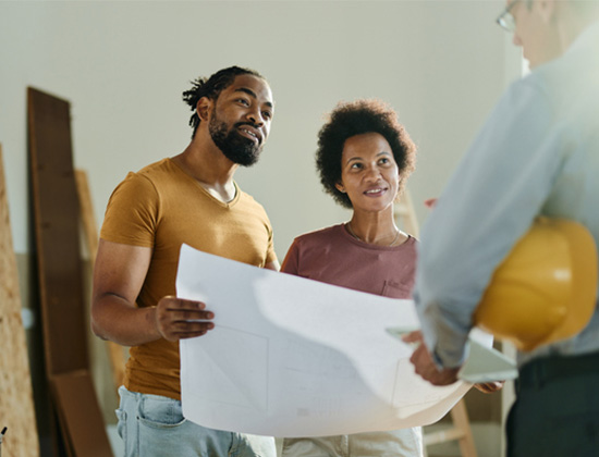 Happy African American couple analyzing blueprints while communicating with a building contractor in the office.