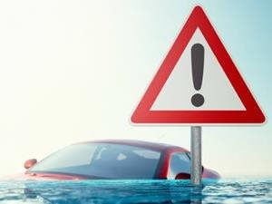 A flooded car submerged in water next to a danger sign.