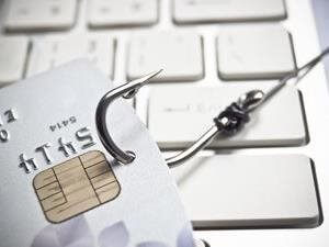 A credit card with a hook attached in front of a computer keyboard to show credit card phishing