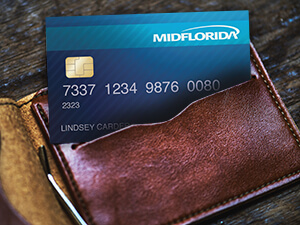 A brown leather wallet with a MIDFLORIDA credit card on a wooden desk