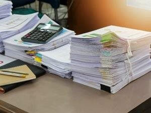 Stacks of reports and documents with a calculator and planner on an office desk